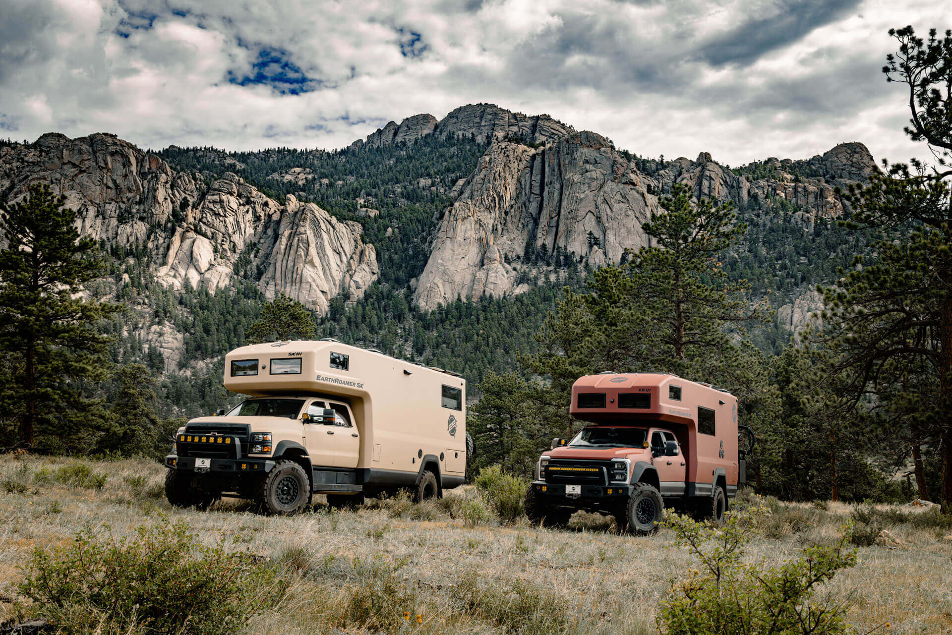 Two EarthRoamer SX expedition vehicles parked in front of rocky mountain cliffs