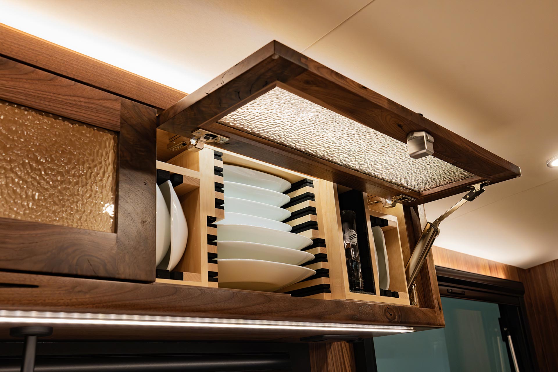 EarthRoamer open cabinet showcasing stacked plates and glassware in custom wood compartments.