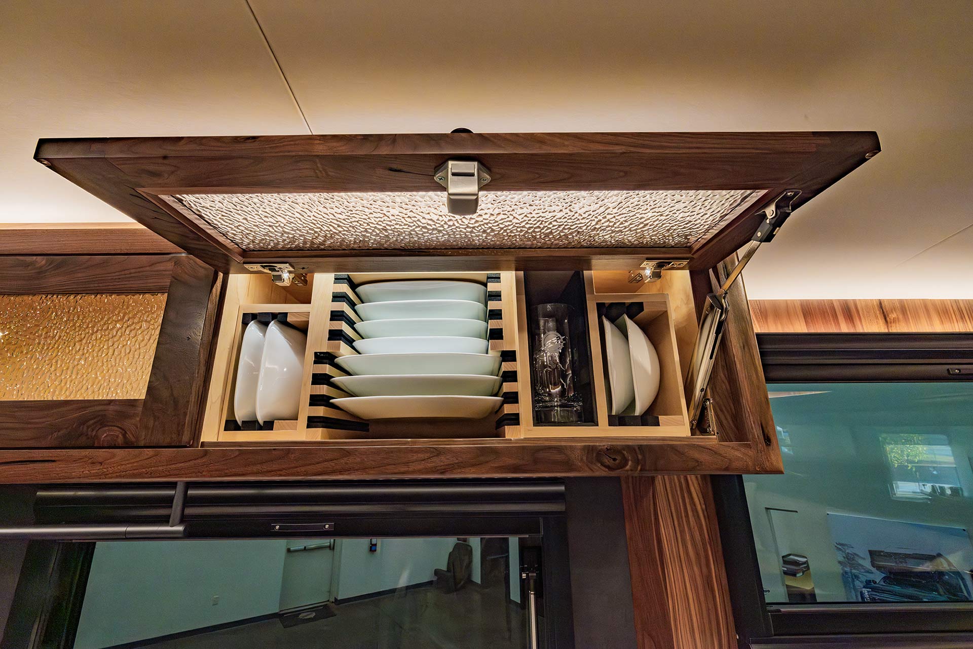 EarthRoamer upper cabinet featuring neatly arranged plates and glasses in secure wooden racks.