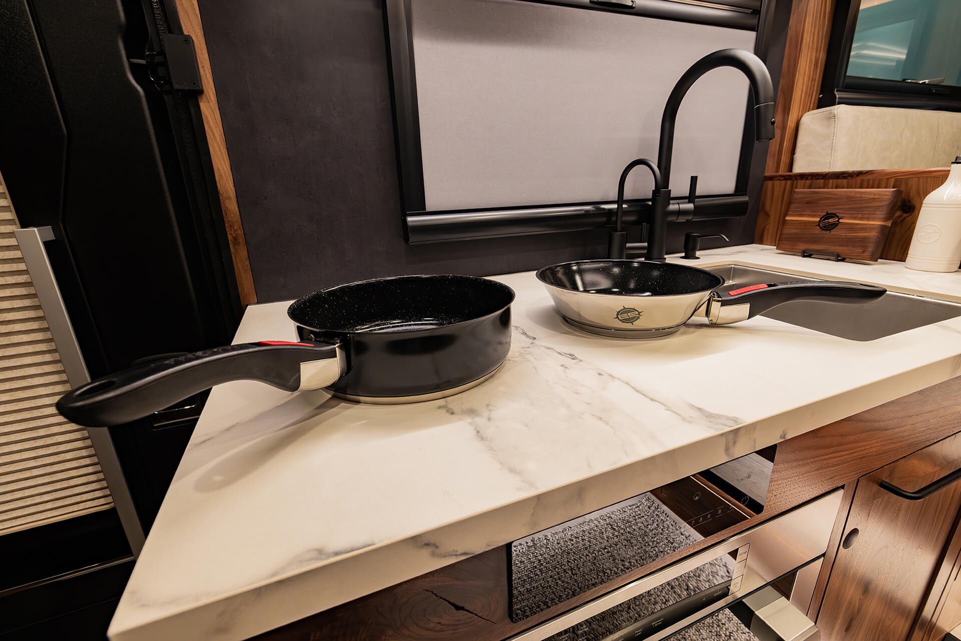 EarthRoamer LTi kitchen counter with two pans on marble surface, faucet, and backsplash.