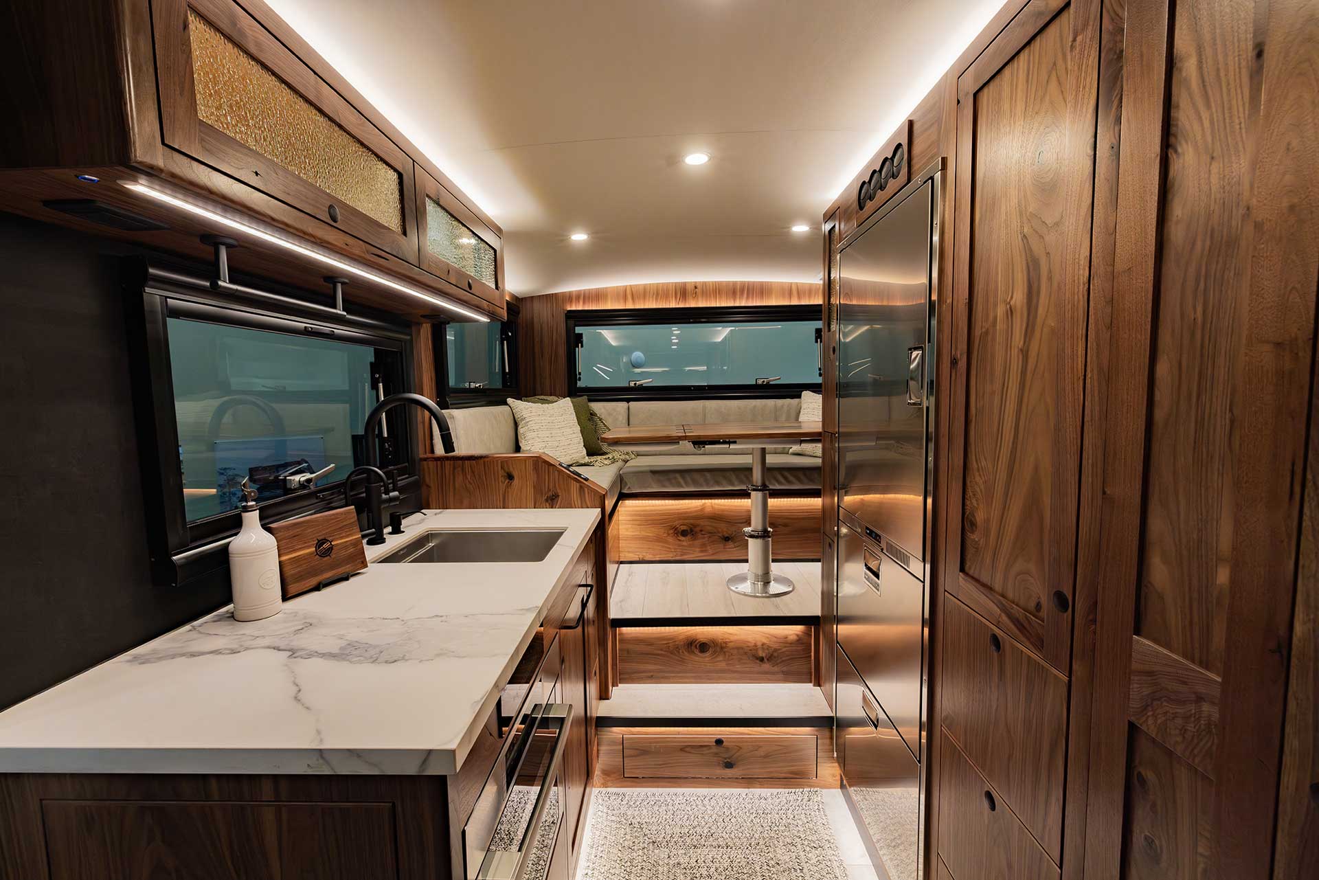 EarthRoamer LTi kitchen with marble countertop, black faucet, wooden cabinets, and modern lighting.