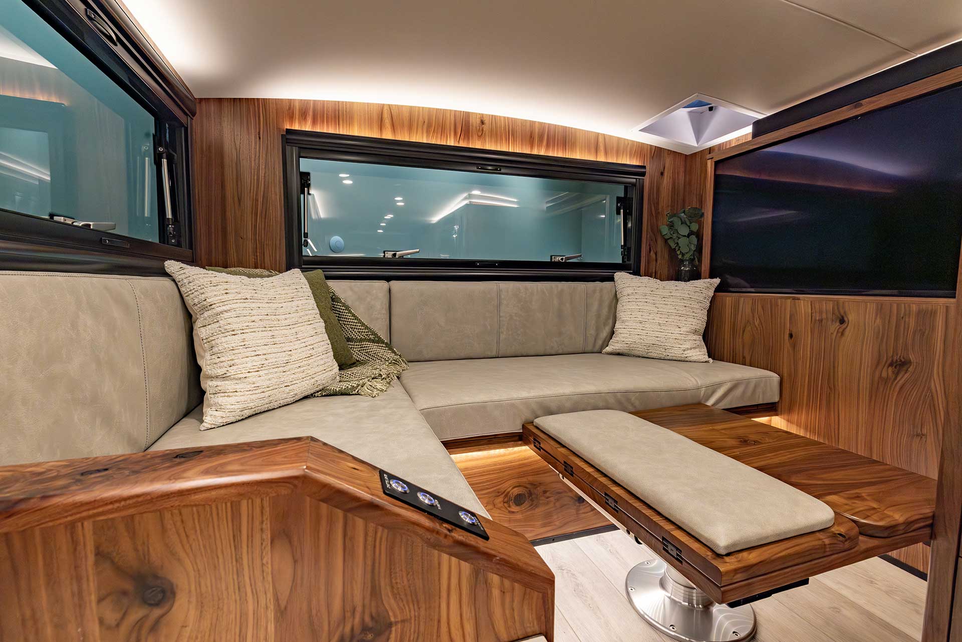EarthRoamer LTi lounge area with L-shaped seating, wood accents, and a mounted TV.