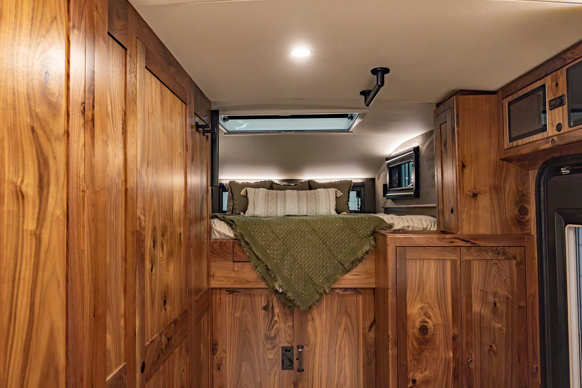 Elevated EarthRoamer LTi bedroom with bed, pillows, and blanket above wooden cabinetry.