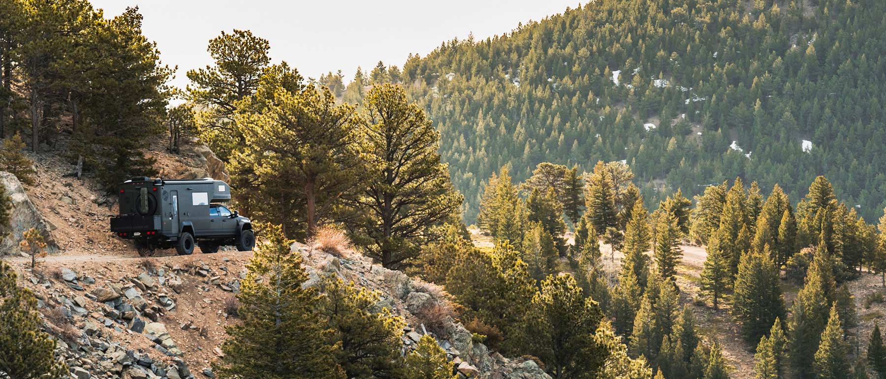 EarthRoamer LTi driving on a rugged mountain trail surrounded by dense pine forest.