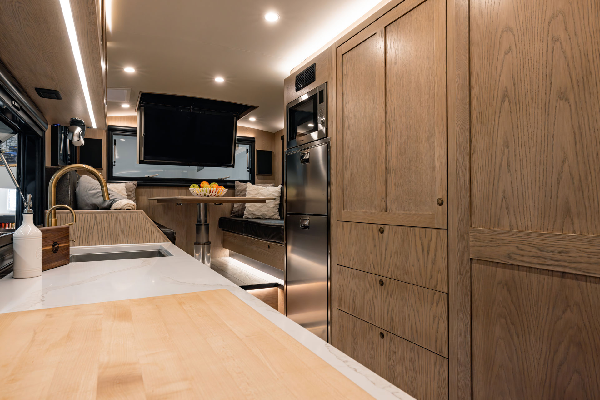 EarthRoamer SX interior showing kitchen counter, fridge, and dining lounge with TV