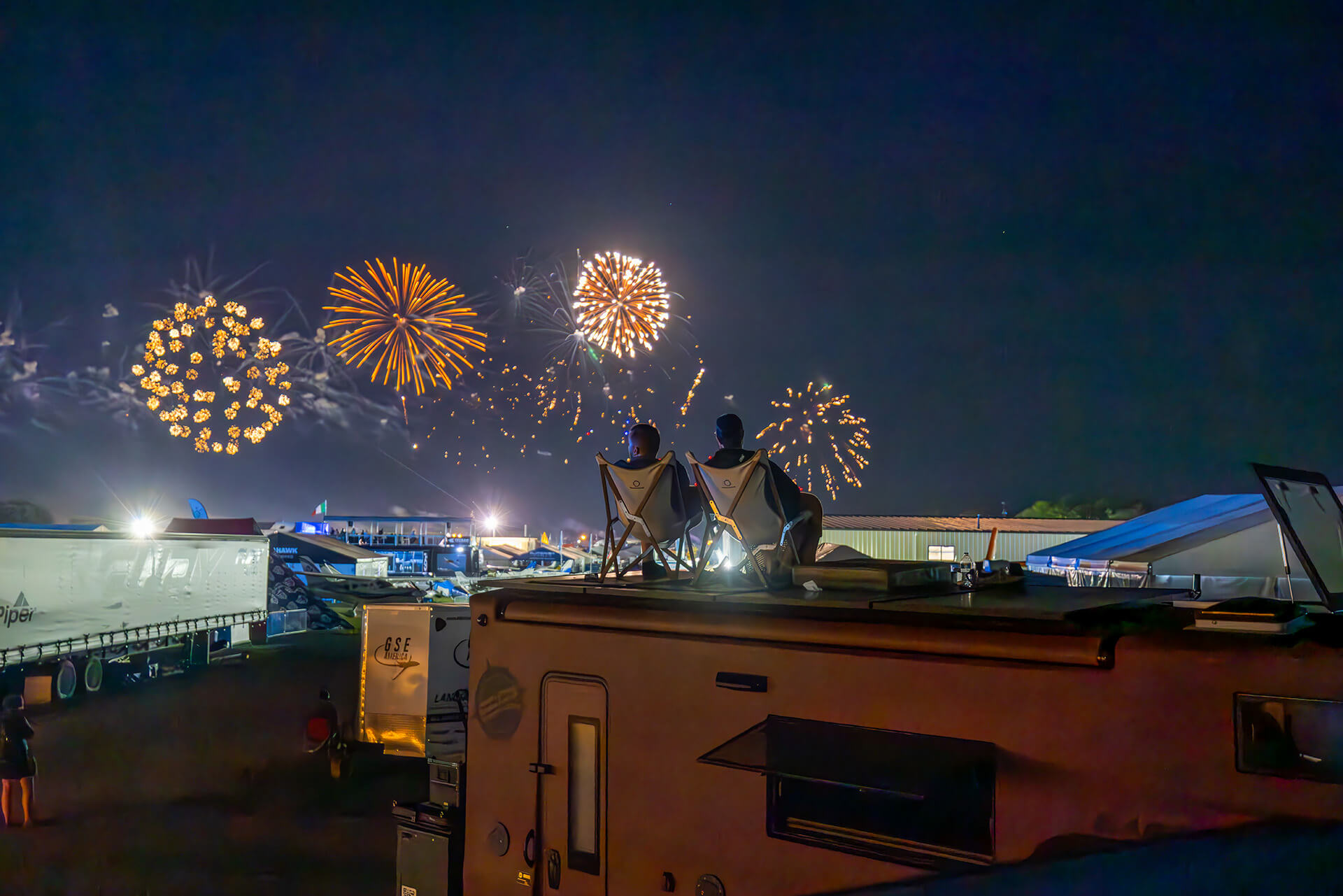 Couple sitting on top of EarthRoamer roof watching colorful fireworks display at night.