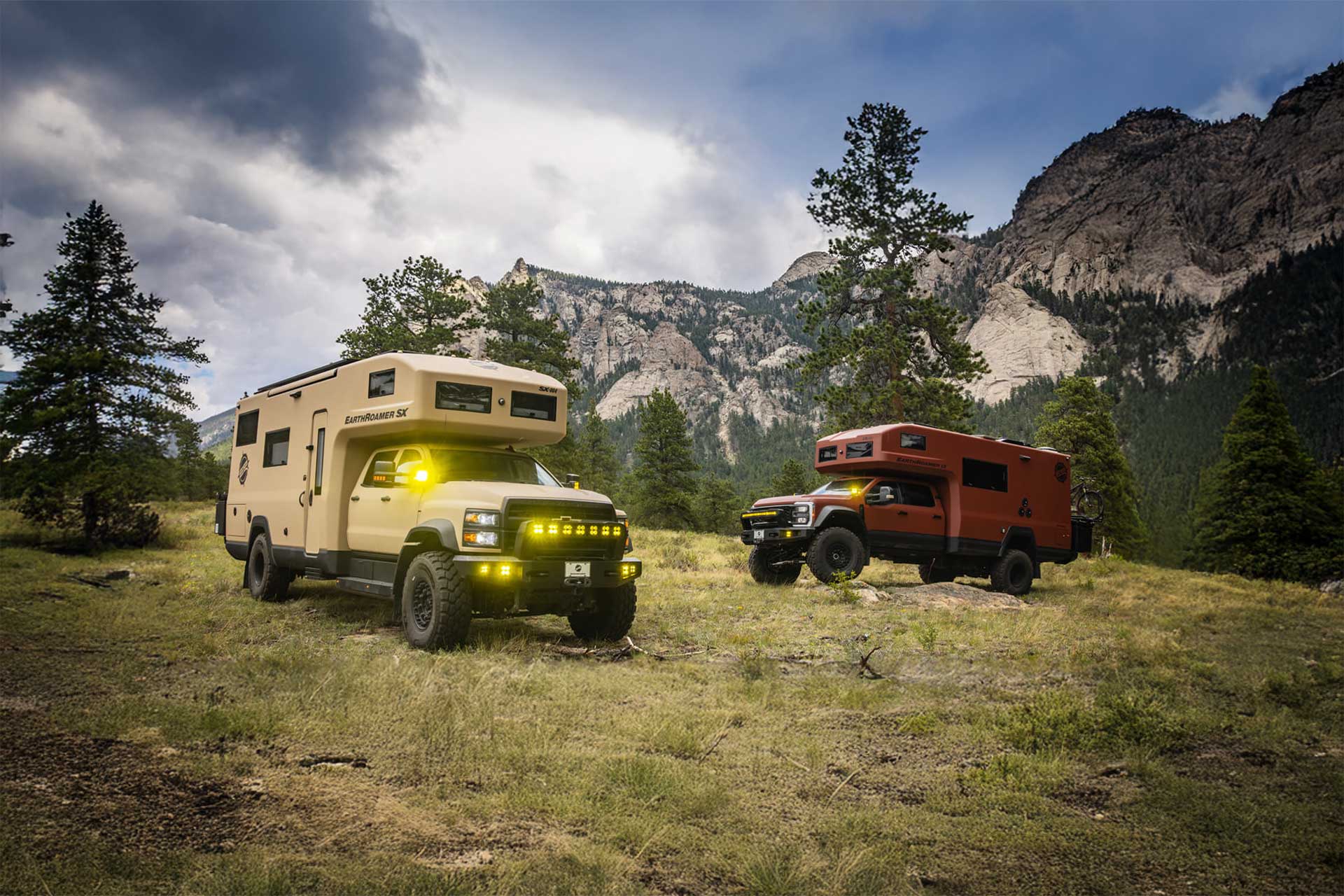 Two EarthRoamer SX expedition vehicles parked in a forest clearing with dramatic mountain backdrop